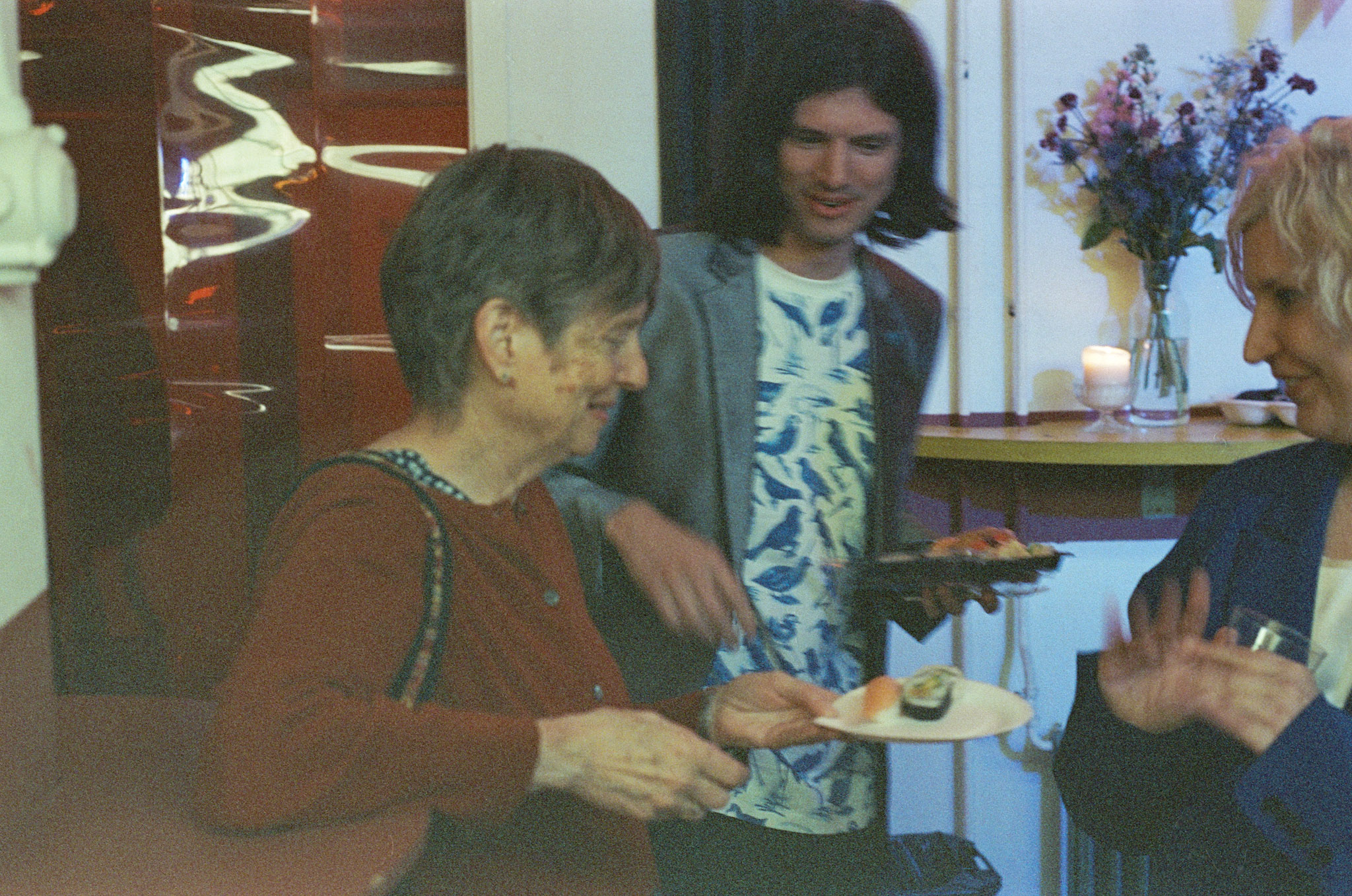 Bill's mom holds a plate of sushi; Eleni smiles to the right
